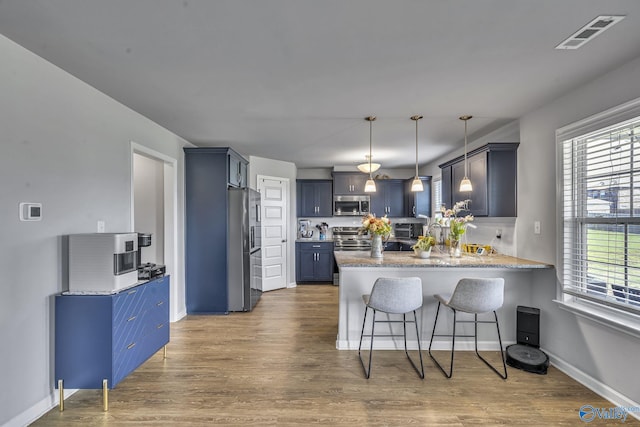 kitchen with decorative light fixtures, a kitchen bar, hardwood / wood-style flooring, kitchen peninsula, and stainless steel appliances