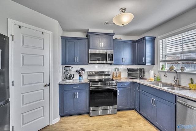 kitchen with light stone countertops, appliances with stainless steel finishes, sink, and blue cabinetry