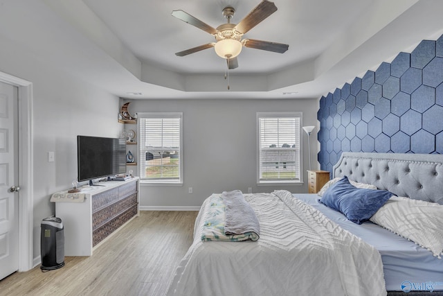 bedroom featuring a raised ceiling, ceiling fan, light wood-type flooring, and multiple windows