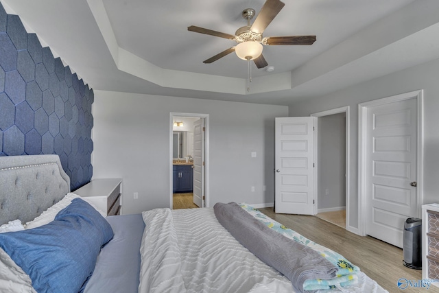 bedroom featuring light hardwood / wood-style flooring, a raised ceiling, ceiling fan, and ensuite bathroom