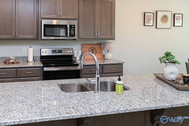 kitchen featuring appliances with stainless steel finishes, dark brown cabinets, light stone countertops, and sink