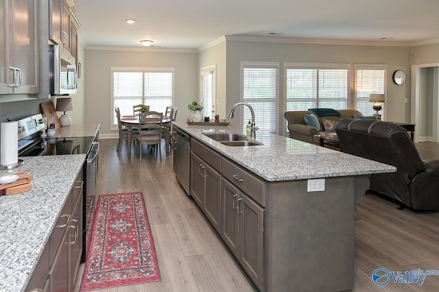 kitchen with an island with sink, sink, light stone countertops, light hardwood / wood-style floors, and appliances with stainless steel finishes