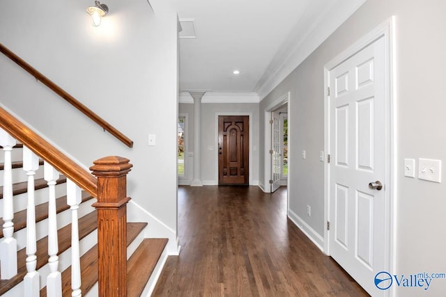 foyer entrance with dark wood-type flooring, a healthy amount of sunlight, crown molding, and decorative columns