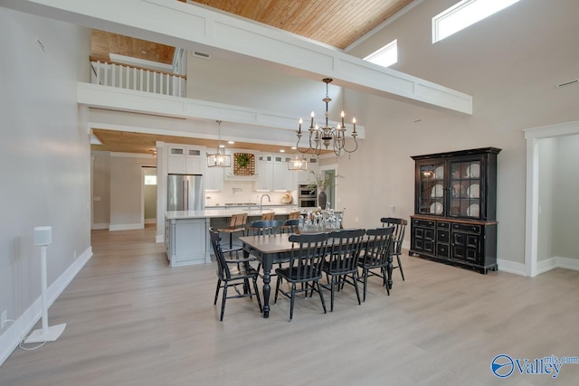 dining space featuring baseboards, a high ceiling, light wood-style flooring, and a notable chandelier