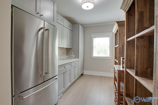 kitchen featuring crown molding, high end fridge, baseboards, light wood-type flooring, and light countertops