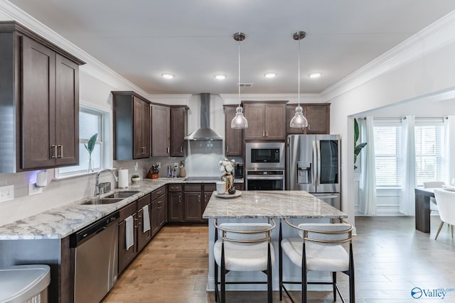 kitchen featuring pendant lighting, a center island, sink, wall chimney exhaust hood, and stainless steel appliances