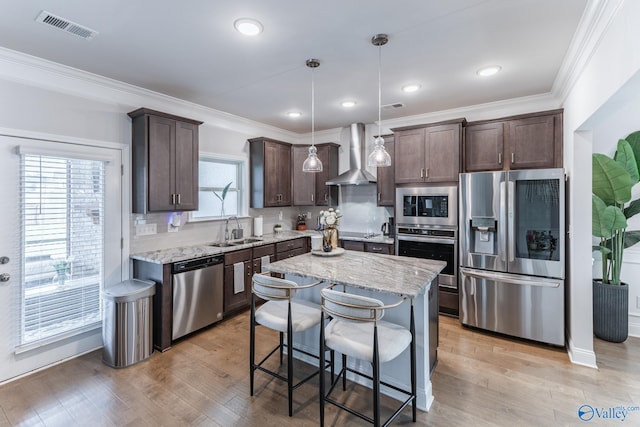 kitchen with wall chimney exhaust hood, stainless steel appliances, a center island, light hardwood / wood-style floors, and hanging light fixtures