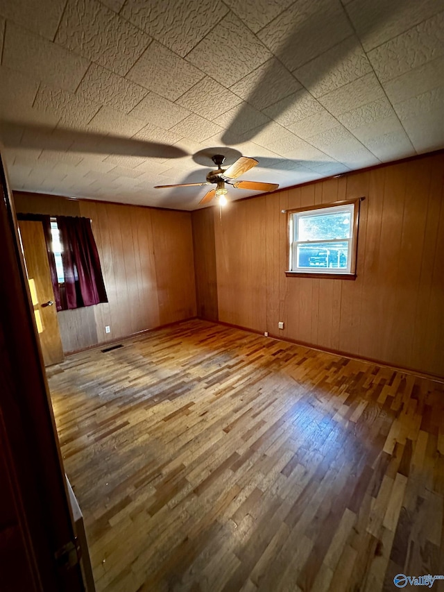 empty room with wooden walls, ceiling fan, and hardwood / wood-style flooring