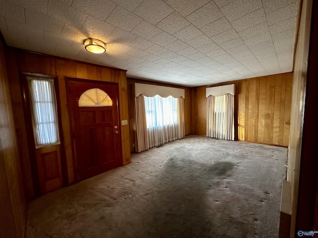 carpeted entrance foyer featuring plenty of natural light and wooden walls