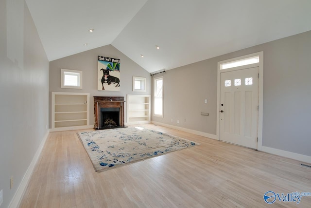 unfurnished living room with built in features, baseboards, light wood finished floors, a fireplace with flush hearth, and a barn door