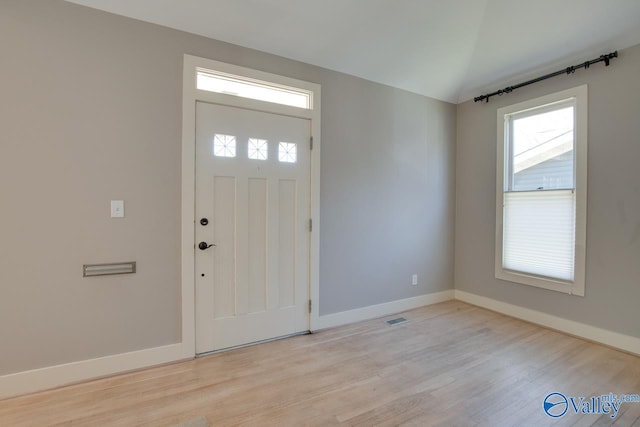 entrance foyer with visible vents, baseboards, vaulted ceiling, and light wood finished floors