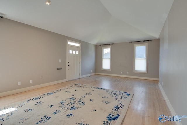 spare room featuring lofted ceiling, light wood-style floors, and baseboards