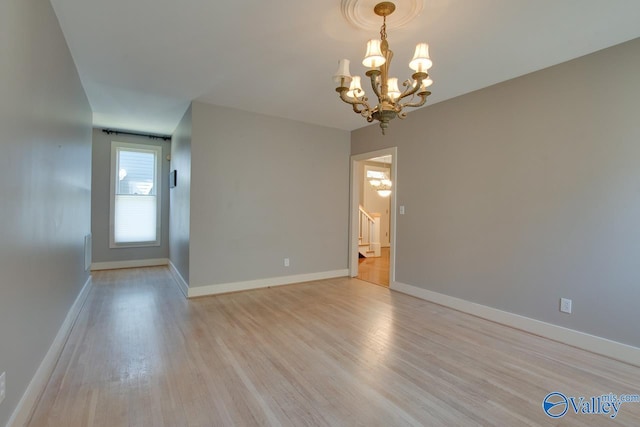 unfurnished room with stairway, an inviting chandelier, baseboards, and light wood-style floors