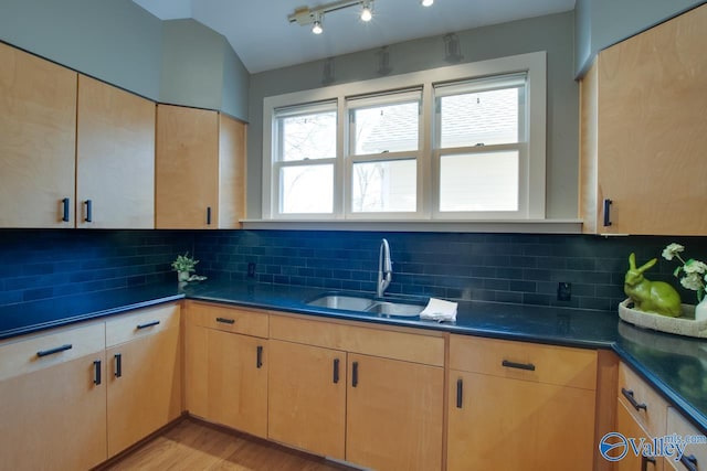 kitchen featuring dark countertops, backsplash, light brown cabinetry, light wood-type flooring, and a sink