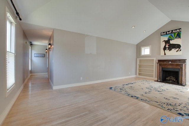 unfurnished living room with light wood finished floors, built in shelves, baseboards, a fireplace, and high vaulted ceiling