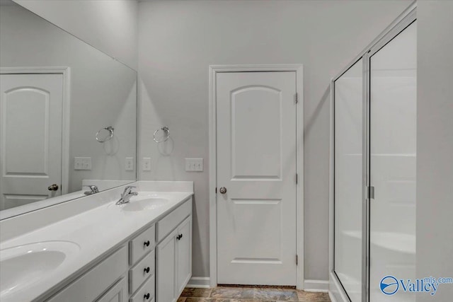 bathroom with double vanity, a shower stall, baseboards, and a sink