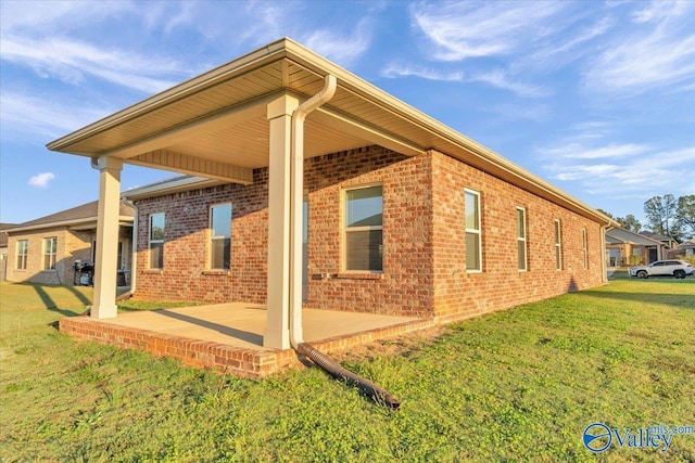 view of home's exterior with brick siding, a yard, and a patio area