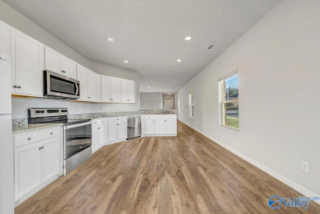 kitchen with a sink, light wood-style flooring, white cabinets, a peninsula, and appliances with stainless steel finishes