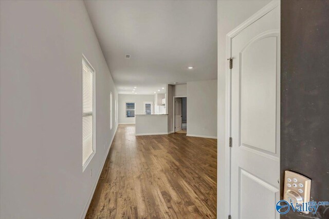 corridor featuring baseboards, wood finished floors, and recessed lighting
