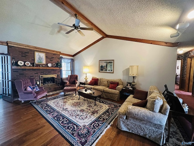 living area featuring vaulted ceiling with beams, wood-type flooring, a brick fireplace, ceiling fan, and a textured ceiling