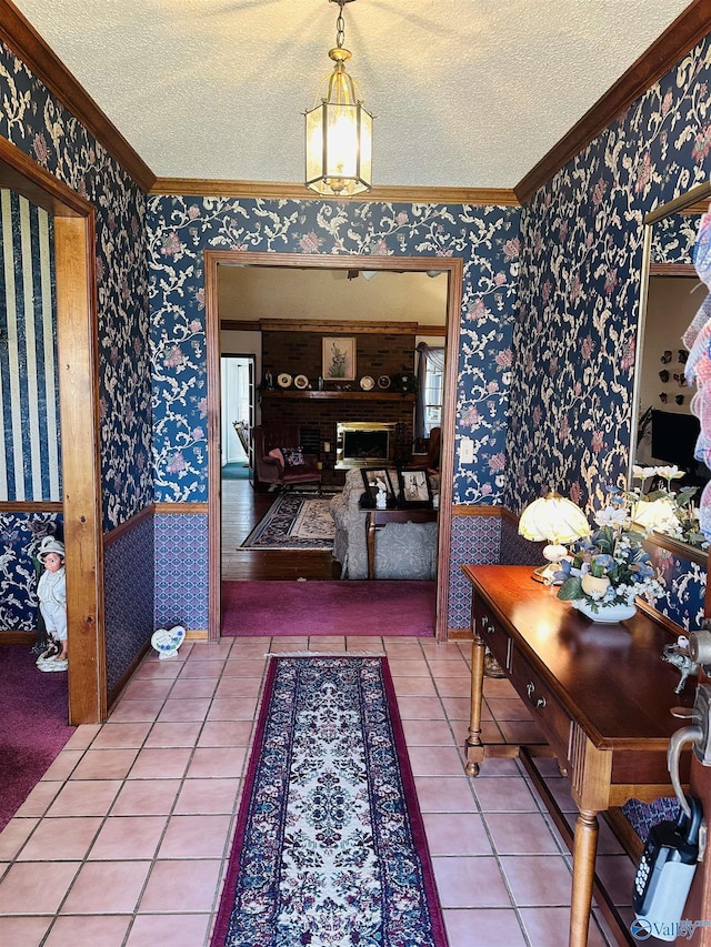 tiled entryway featuring wallpapered walls, ornamental molding, a textured ceiling, and wainscoting