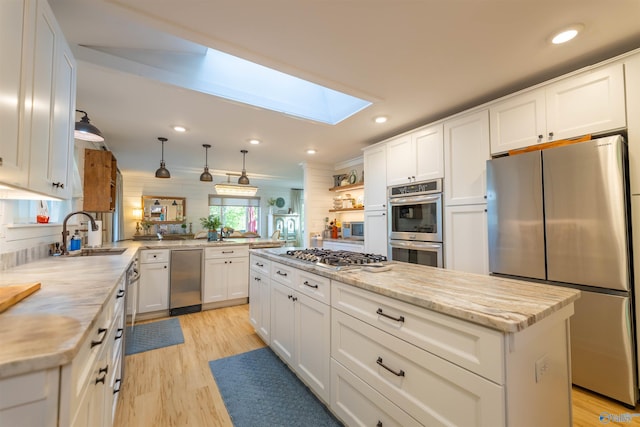 kitchen featuring a skylight, stainless steel appliances, a sink, and white cabinetry