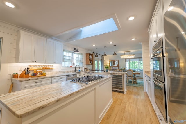 kitchen with light wood finished floors, a peninsula, stainless steel appliances, a kitchen island, and beverage cooler