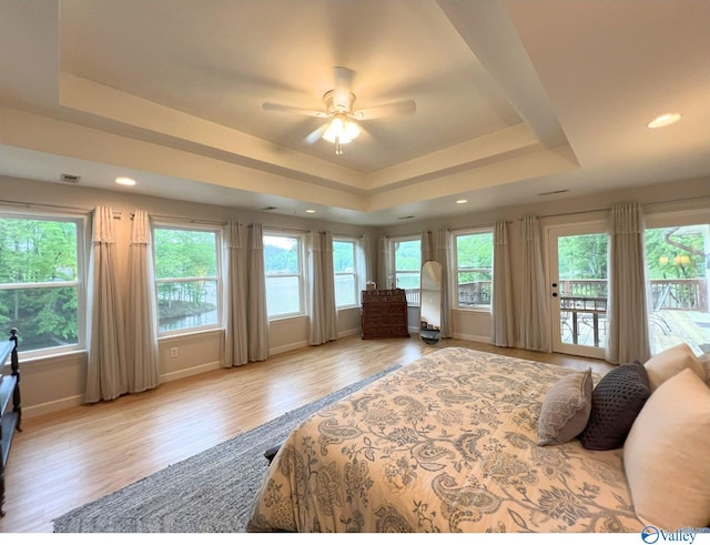 bedroom featuring access to outside, wood finished floors, multiple windows, and a raised ceiling