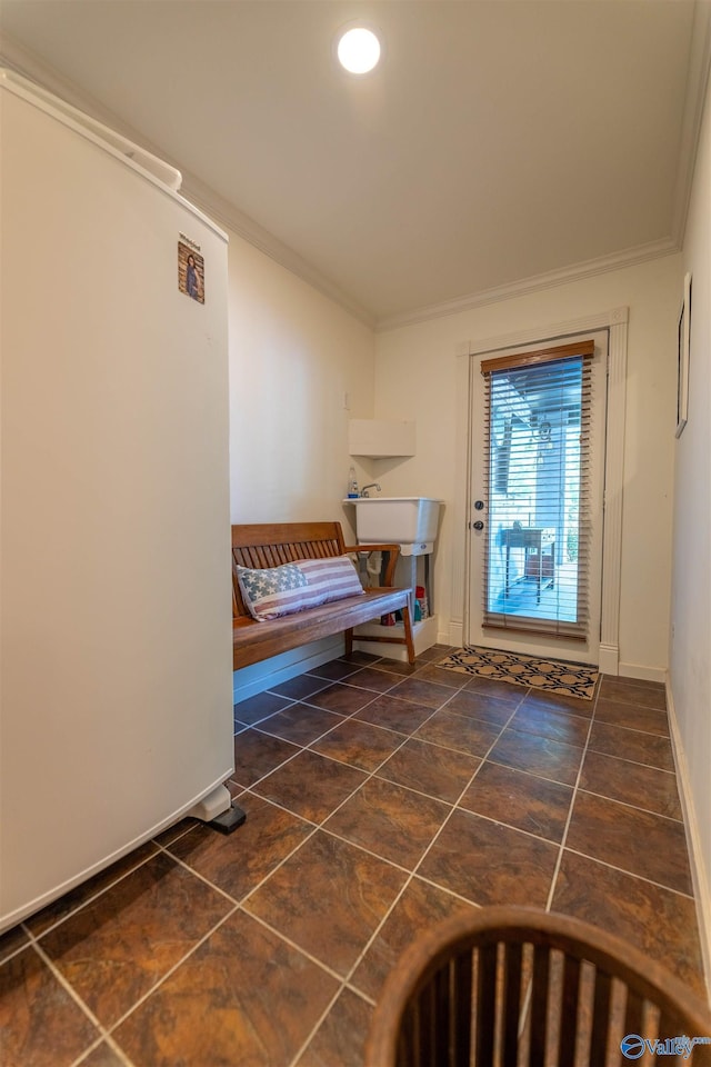 doorway with crown molding, baseboards, a sink, and tile patterned floors