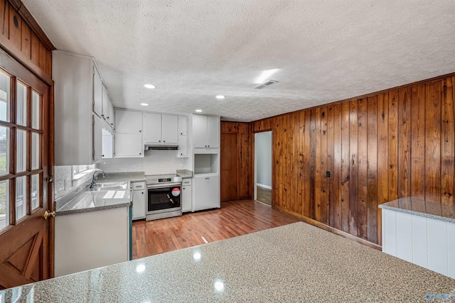 kitchen featuring white cabinetry, stainless steel electric range oven, sink, light hardwood / wood-style flooring, and wood walls