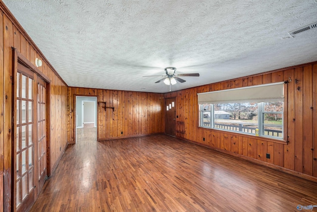 spare room featuring a textured ceiling, ceiling fan, dark wood-type flooring, and wood walls