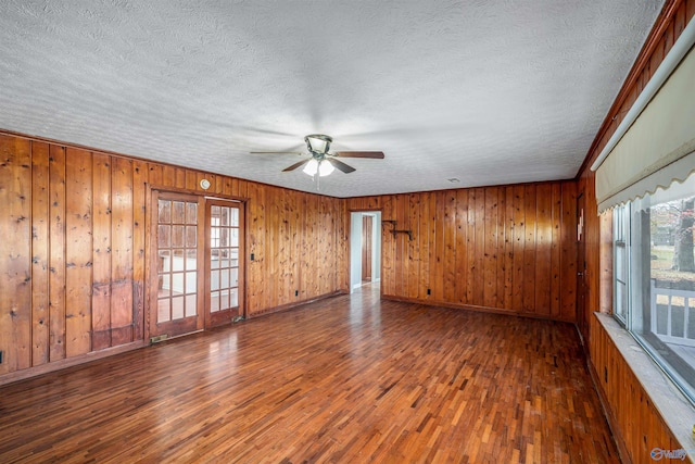 unfurnished room featuring dark hardwood / wood-style floors, wood walls, a textured ceiling, and ceiling fan