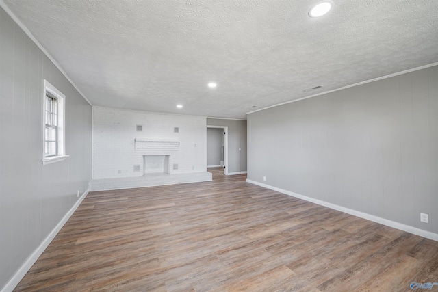 unfurnished living room with wood-type flooring, a textured ceiling, and a brick fireplace