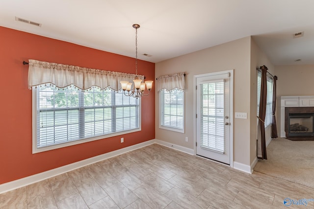 unfurnished dining area with an inviting chandelier, a tiled fireplace, and light carpet