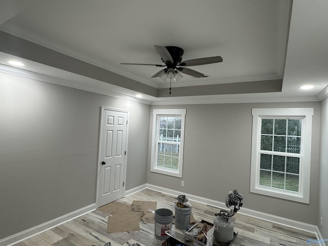 workout area featuring a raised ceiling, ceiling fan, light wood-type flooring, and ornamental molding