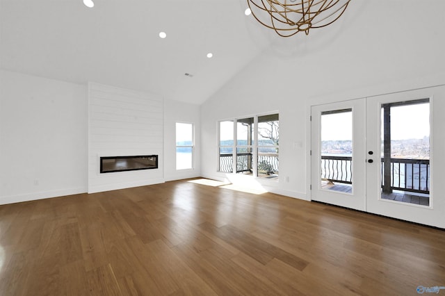 unfurnished living room featuring high vaulted ceiling, wood-type flooring, a large fireplace, a chandelier, and french doors