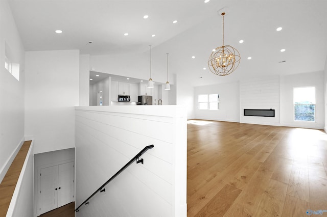 staircase with an inviting chandelier, hardwood / wood-style floors, a fireplace, and high vaulted ceiling