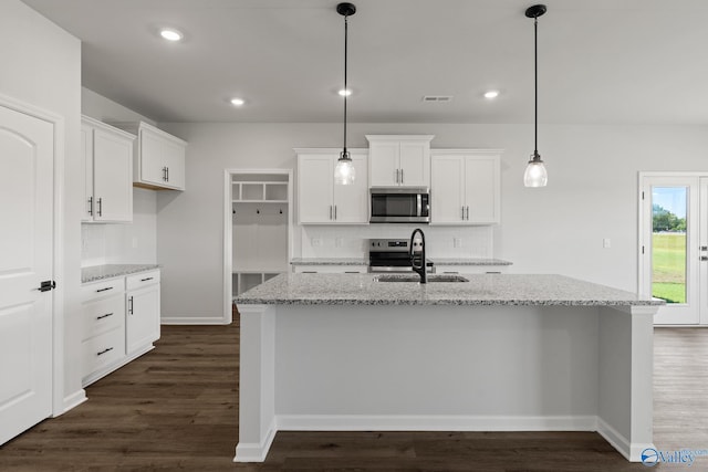 kitchen with light stone counters, stainless steel appliances, a kitchen island with sink, and hanging light fixtures