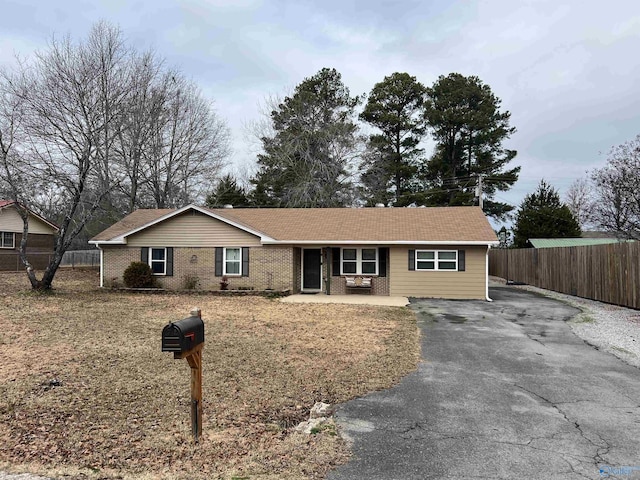 ranch-style home with aphalt driveway, brick siding, fence, and a patio