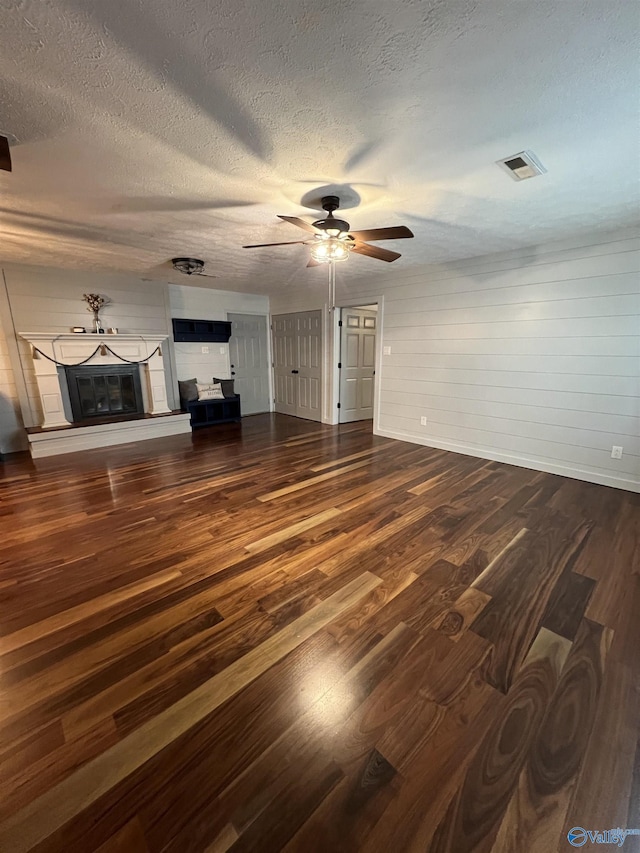 unfurnished living room with a glass covered fireplace, visible vents, dark wood finished floors, and a textured ceiling