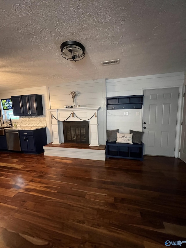 unfurnished living room featuring a glass covered fireplace, visible vents, dark wood finished floors, and a sink