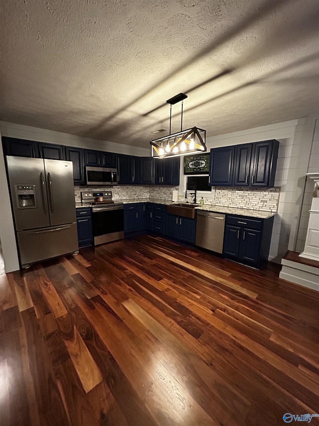 kitchen with dark wood-style floors, light countertops, hanging light fixtures, appliances with stainless steel finishes, and a sink