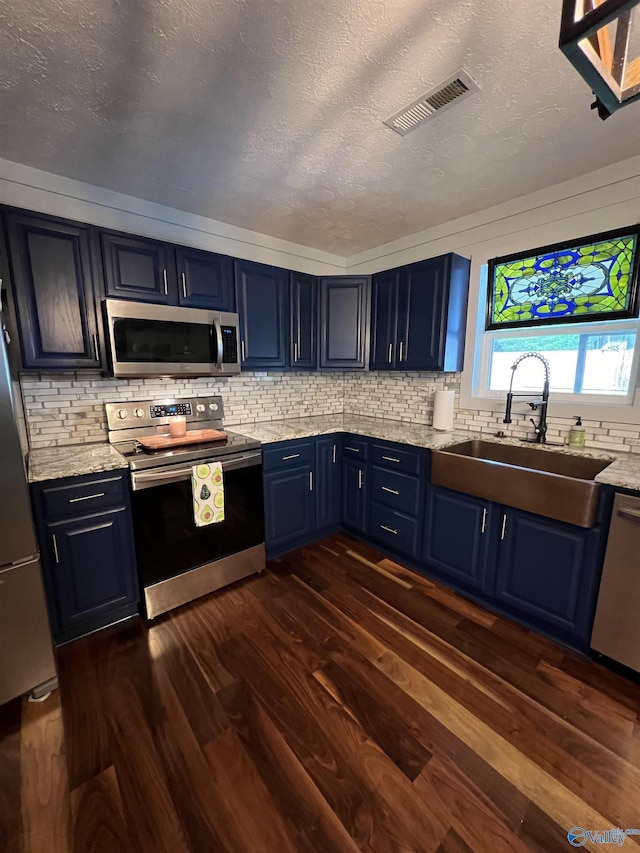 kitchen with blue cabinets, dark wood-type flooring, a sink, visible vents, and appliances with stainless steel finishes