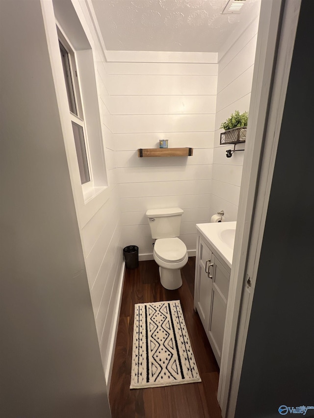 half bath featuring toilet, a textured ceiling, wood finished floors, and vanity