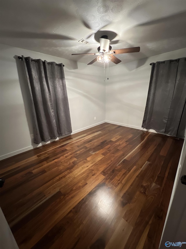 empty room with dark wood-style flooring, visible vents, ceiling fan, and baseboards