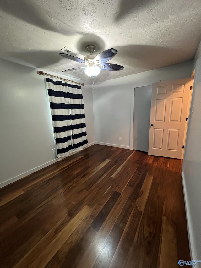 empty room featuring ceiling fan, a textured ceiling, baseboards, and dark wood-style flooring