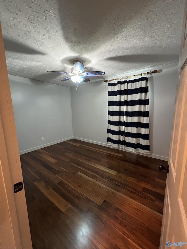 unfurnished room with a ceiling fan, dark wood-style flooring, a textured ceiling, and baseboards