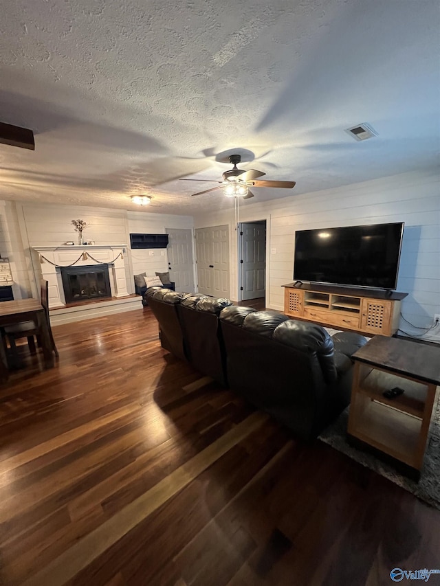 living area with a textured ceiling, ceiling fan, wood finished floors, visible vents, and a glass covered fireplace