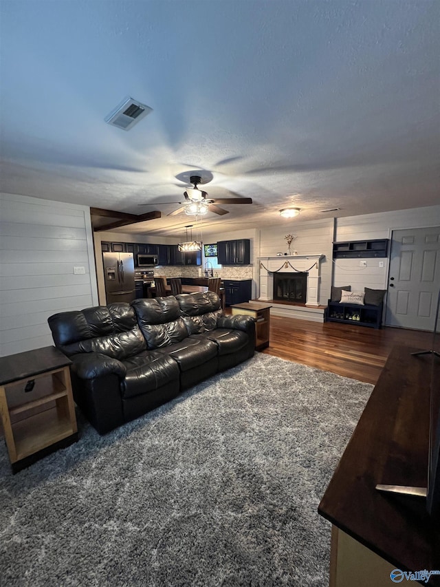 living area with a fireplace with raised hearth, a textured ceiling, dark wood-style flooring, visible vents, and a ceiling fan