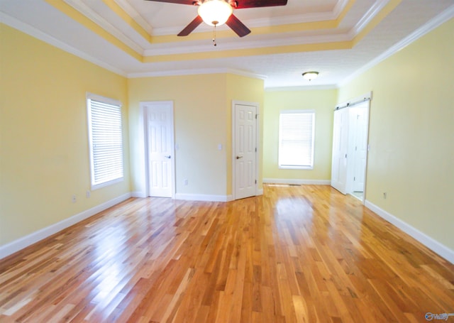 empty room with light hardwood / wood-style flooring, a raised ceiling, crown molding, and a barn door